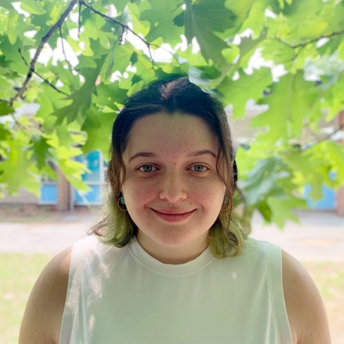 Emily Olsen, an educator at Belmont BASEC, smiles standing under the trees