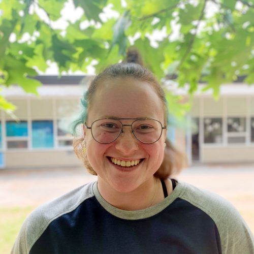 Meg Mayfield, an educator at Belmont BASEC, smiles standing under the trees